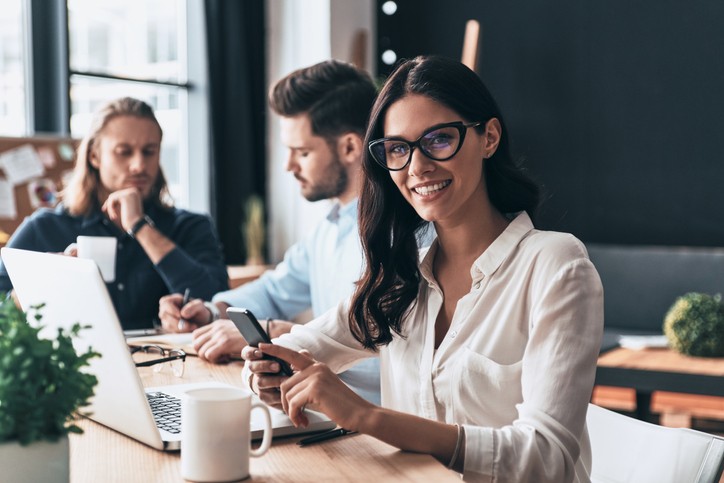 Jovens colegas modernos em roupas casuais inteligentes trabalhando enquanto passam o tempo no escritório. Empresária aplicando uma boa gestão empresarial.