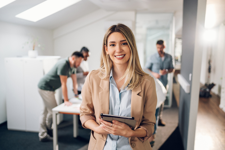 Sorrindo confiante líder empresarial olhando para a câmera e de pé em um escritório na reunião da equipe. Retrato de empresária confiante com colegas na sala de reuniões. Posando enquanto segura o tablet digital. Uma boa liderança faz toda a diferença.