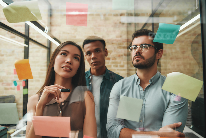 Sessão de brainstorming sobre empreendedorismo. Alegres colegas masculinos e femininos planejando o processo de trabalho e usando adesivos em pé no escritório moderno. Trabalho em equipe. Gerenciamento de projetos