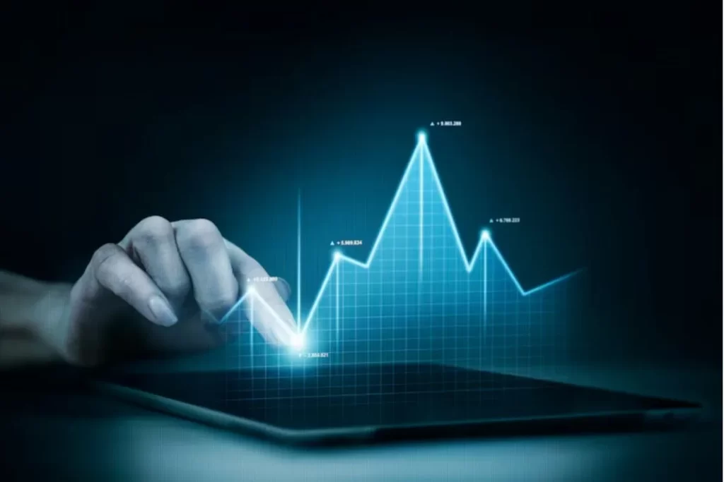 Mão interagindo com uma tela digital, visualizando um gráfico de mercado financeiro, representando o crescimento e volatilidade no mercado de ações.