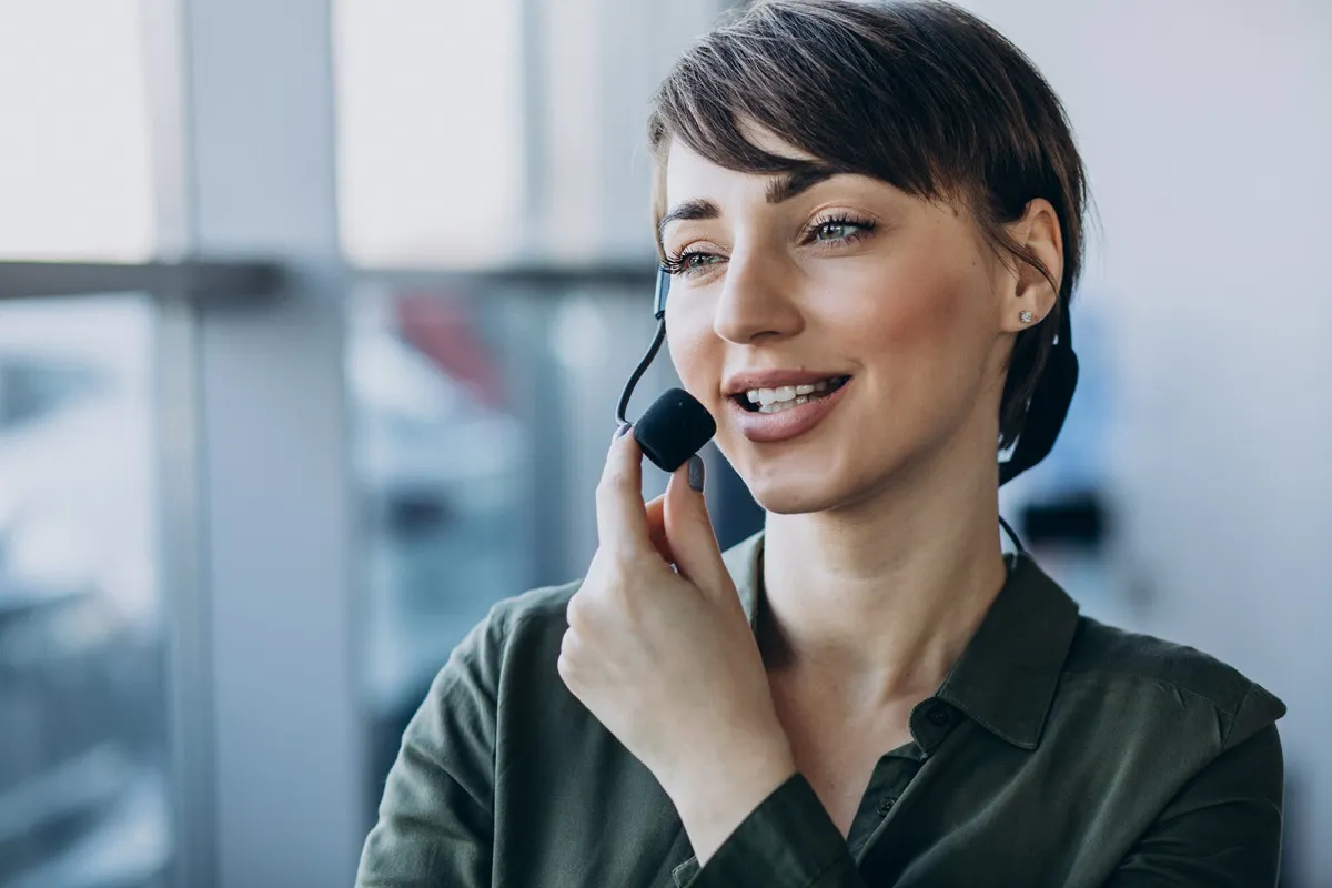 Mulher profissional com headset sorrindo enquanto realiza atendimento ao cliente em ambiente corporativo