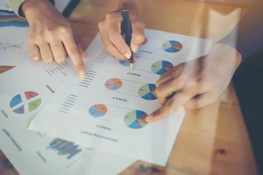 Mãos apontando gráficos e diagramas coloridos em papéis, representando a análise de dados para benchmarking.