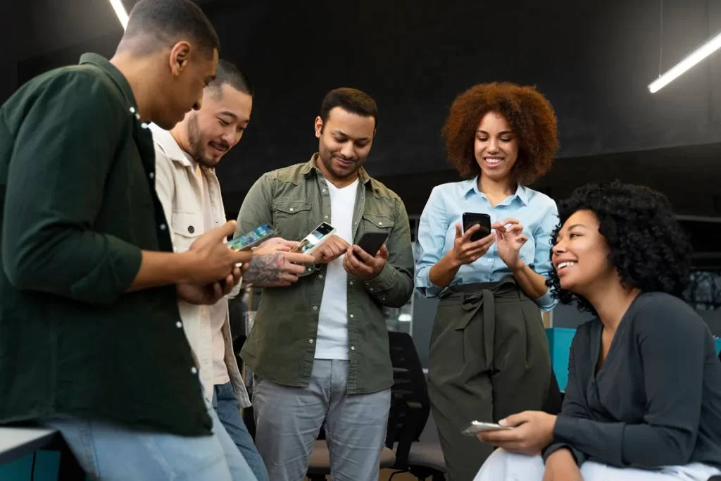 Grupo de pessoas diversas interagindo com smartphones em um ambiente corporativo, representando engajamento e comunicação em equipe.