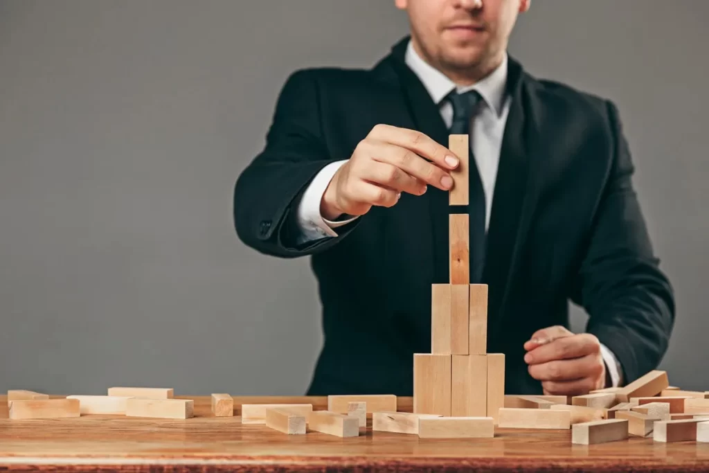 Homem de terno montando uma estrutura de blocos de madeira em uma mesa, representando o conceito de planejamento estratégico no funil de vendas.