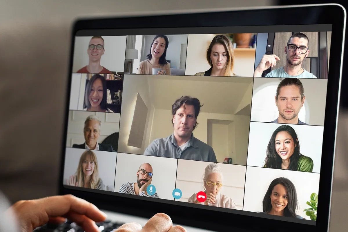 Tela de laptop mostrando uma reunião virtual em videoconferência com várias pessoas.